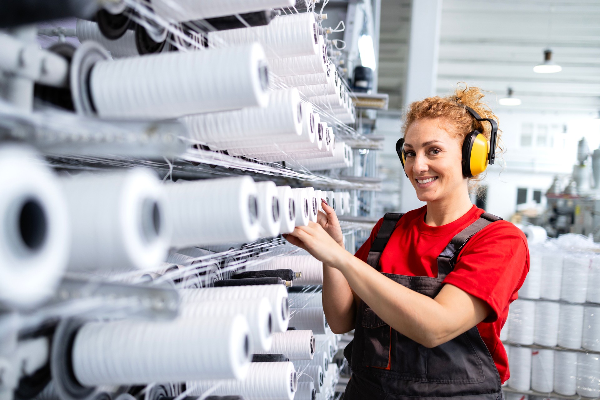 Female employee working in textile factory checking industrial sewing machine.